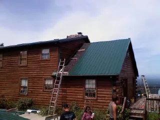 Green metal roof going on a two story log home with ladders set in Washington